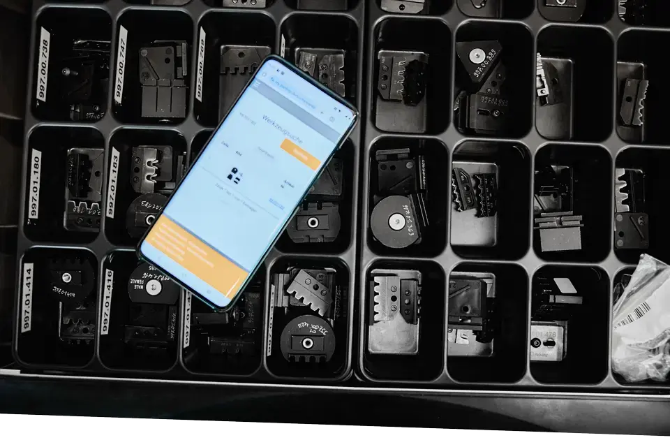 Smartphone auf Crimpwerkzeug-Sortiment mit interner Web-App zur Komponentensuche bei Pahling